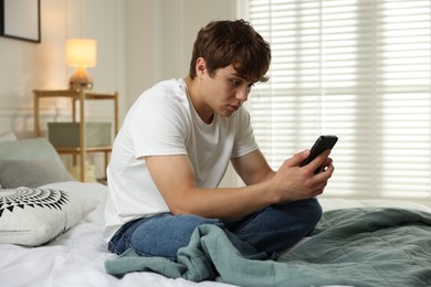 Photo of Teen problems. Upset teenage boy with smartphone on bed at home
