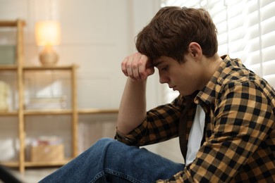 Photo of Teen problems. Depressed teenage boy near window at home, space for text