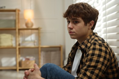 Photo of Teen problems. Depressed teenage boy near window at home, space for text