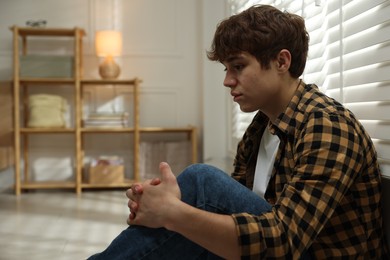 Photo of Teen problems. Depressed teenage boy near window at home, space for text