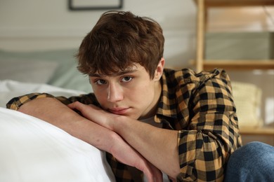 Photo of Teen problems. Upset teenage boy near bed at home
