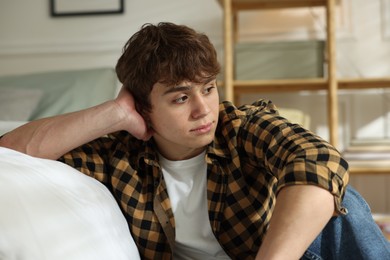 Photo of Teen problems. Upset teenage boy near bed at home
