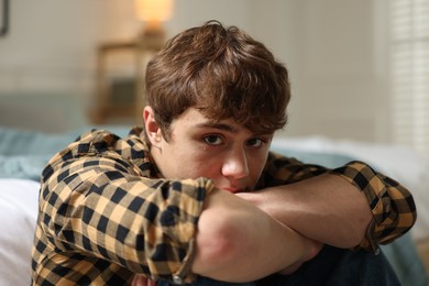 Photo of Teen problems. Upset teenage boy near bed at home