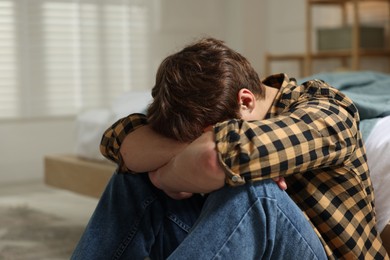 Photo of Teen problems. Depressed teenage boy near bed at home