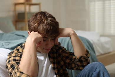 Photo of Teen problems. Depressed teenage boy near bed at home