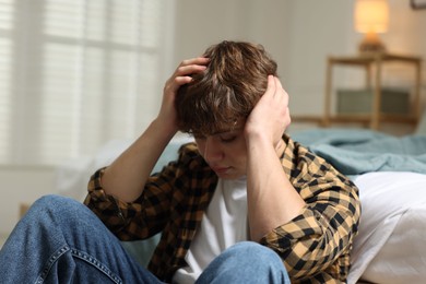 Photo of Teen problems. Depressed teenage boy near bed at home