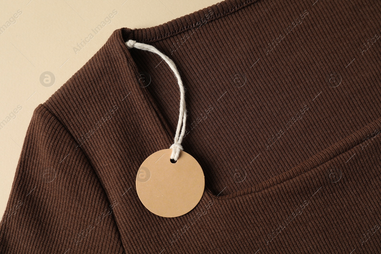 Brown garment with tag on beige background, top view Photo of Brown garment with tag on beige background, top view