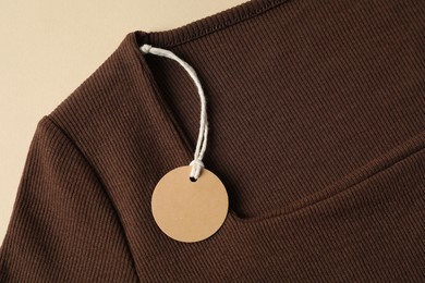 Photo of Brown garment with tag on beige background, top view