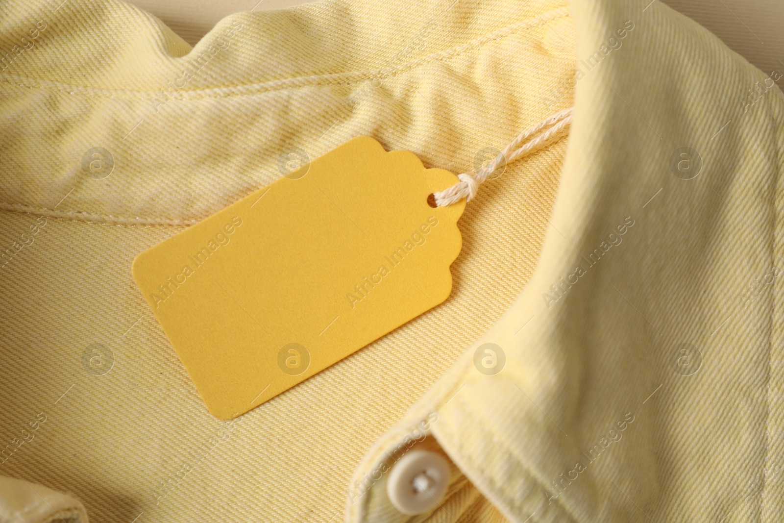 Cardboard tag on pale yellow shirt, top view Photo of Cardboard tag on pale yellow shirt, top view