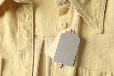 Photo of Cardboard tags on pale yellow shirt, top view