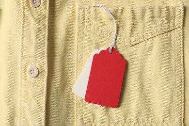Photo of Cardboard tags on pale yellow shirt, top view