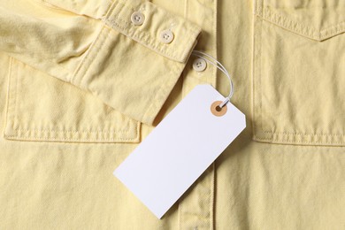 Photo of Cardboard tag on pale yellow shirt, top view