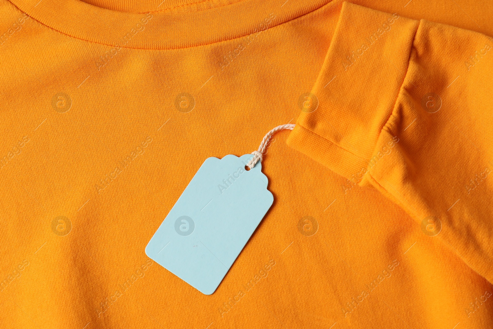 Cardboard tag on orange garment, top view Photo of Cardboard tag on orange garment, top view