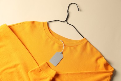 Photo of Orange garment with tag on beige background, top view