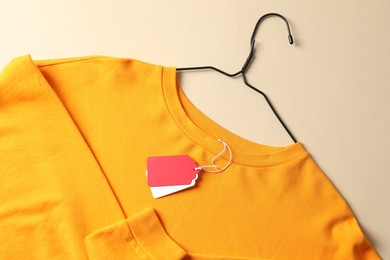 Photo of Orange garment with tags on beige background, top view
