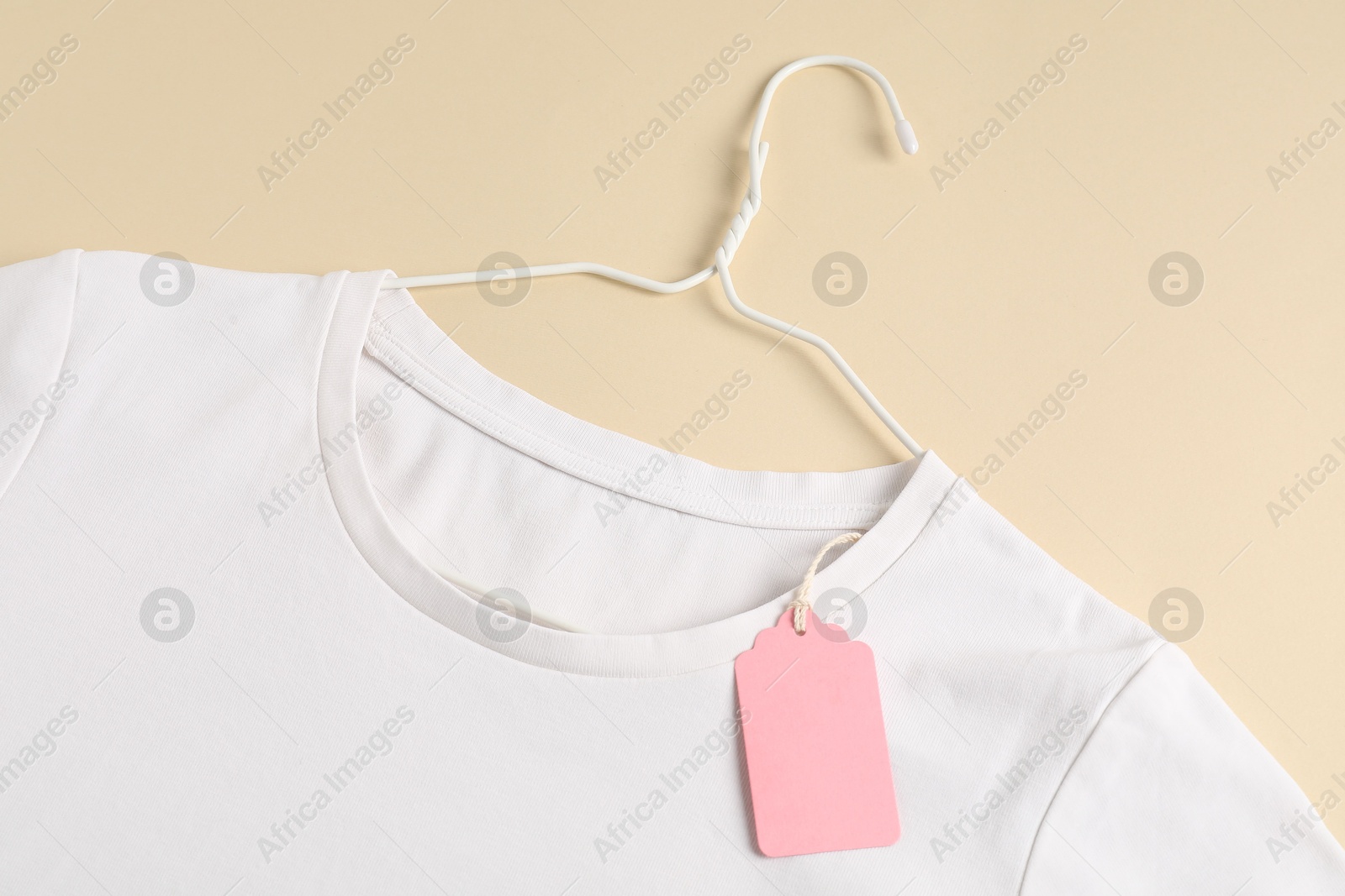 Photo of White t-shirt with tag on beige background, top view