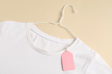 Photo of White t-shirt with tag on beige background, top view