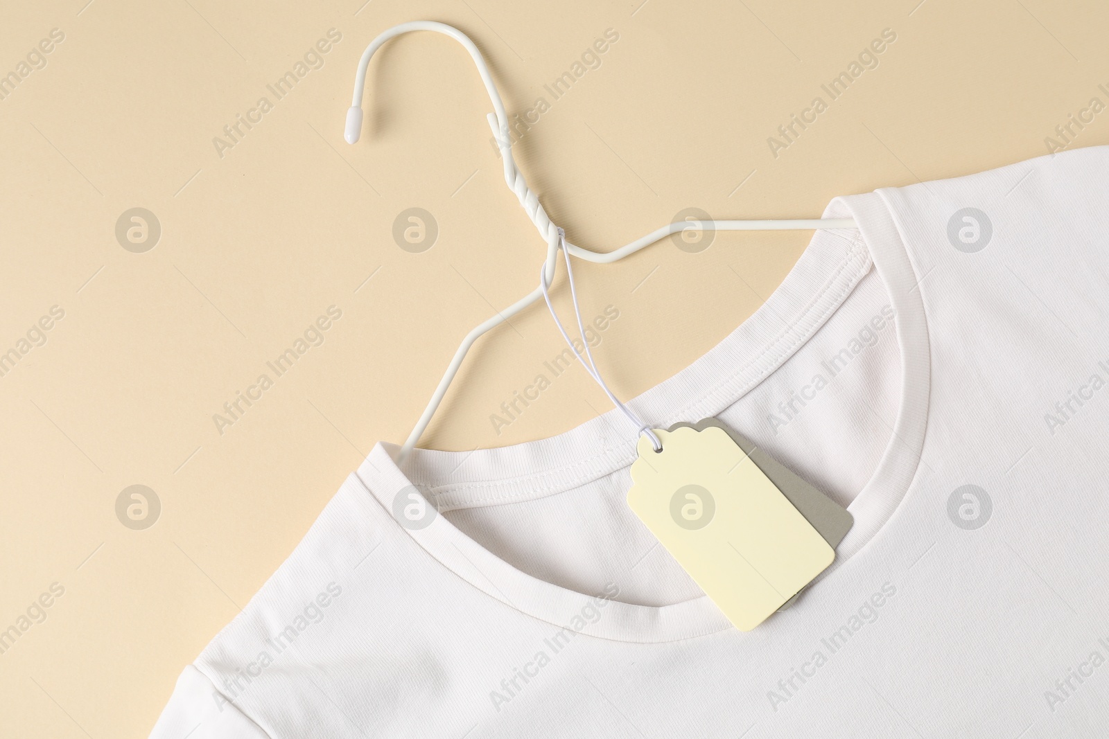 White t-shirt with tag on beige background, top view Photo of White t-shirt with tag on beige background, top view