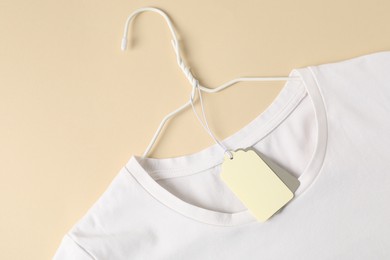 Photo of White t-shirt with tag on beige background, top view