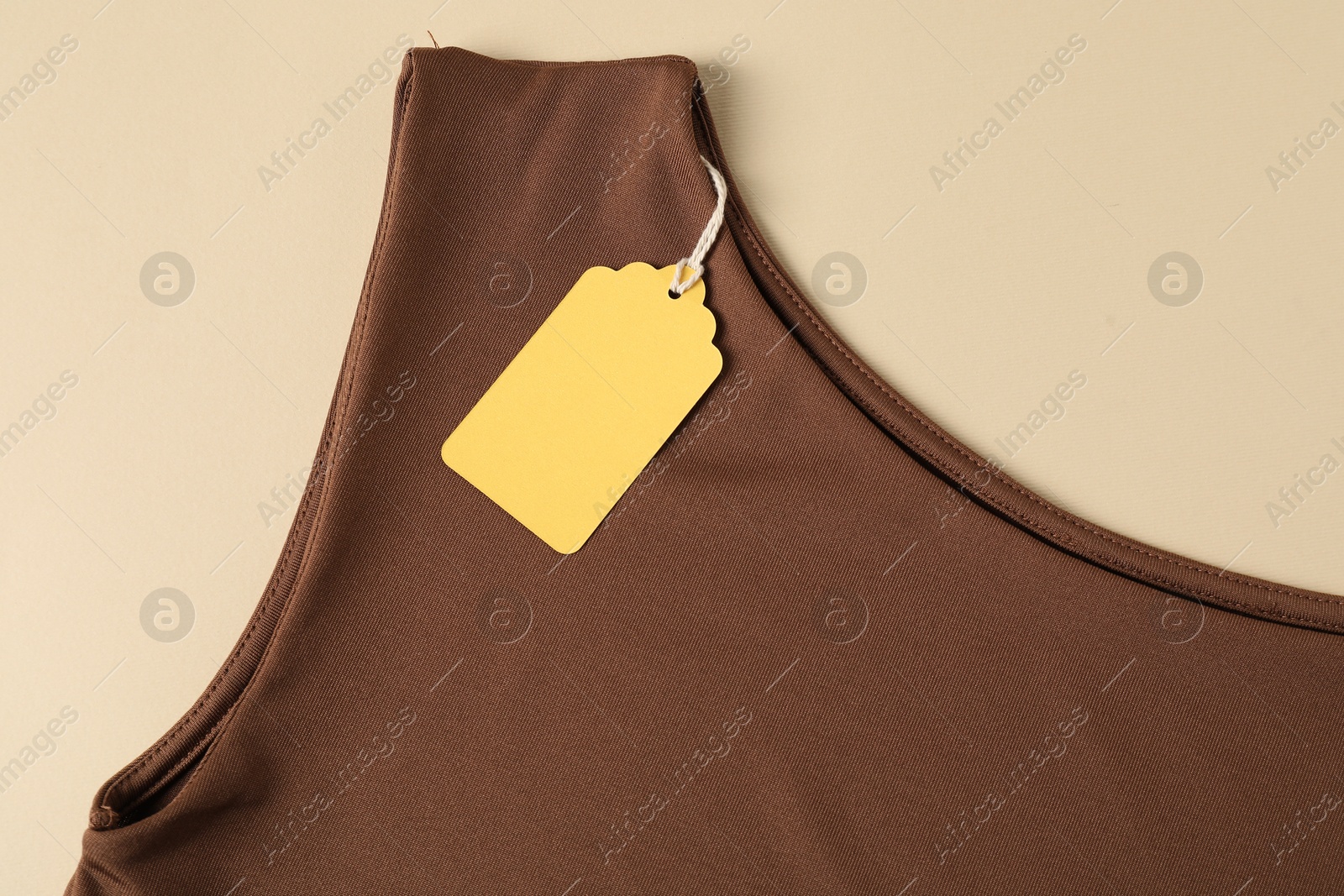 Brown garment with tag on beige background, top view Photo of Brown garment with tag on beige background, top view