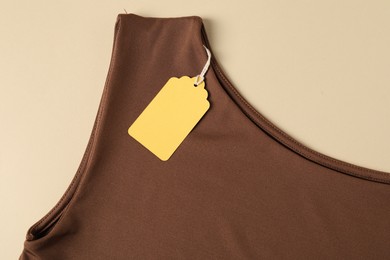 Photo of Brown garment with tag on beige background, top view