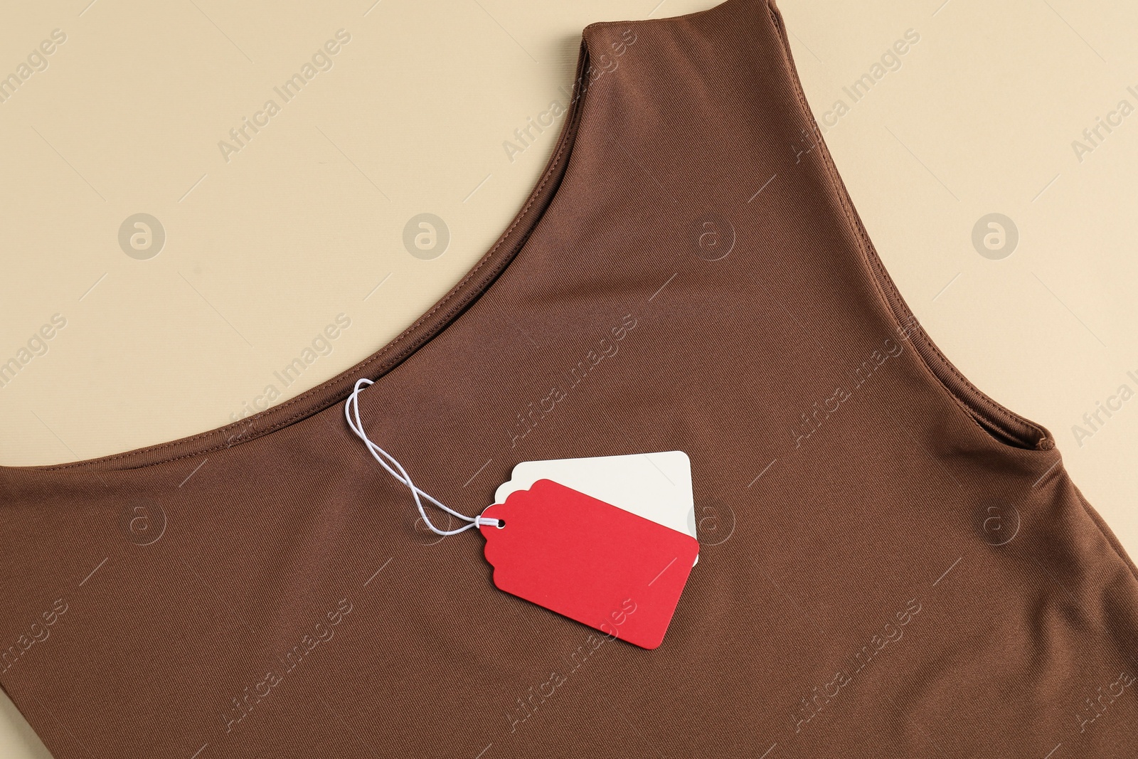 Brown garment with tags on beige background, top view Photo of Brown garment with tags on beige background, top view
