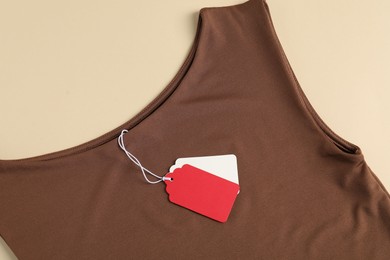 Photo of Brown garment with tags on beige background, top view