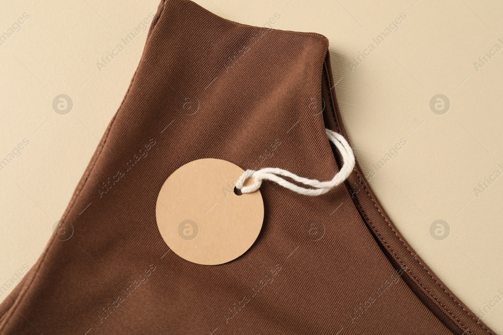 Brown garment with tag on beige background, top view Photo of Brown garment with tag on beige background, top view