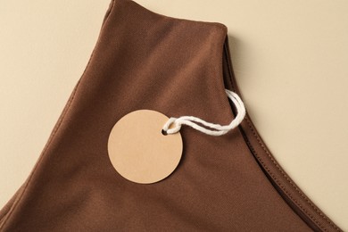 Photo of Brown garment with tag on beige background, top view