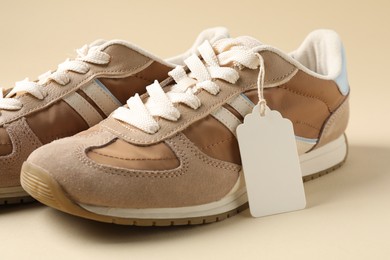 Photo of Pair of sneakers with tag on beige background, closeup