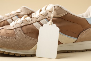 Photo of Pair of sneakers with tag on beige background, closeup