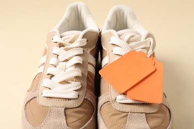 Photo of Pair of sneakers with tags on beige background, closeup