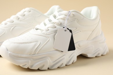 Photo of Pair of sneakers with tags on beige background, closeup