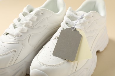 Photo of Pair of sneakers with tags on beige background, closeup