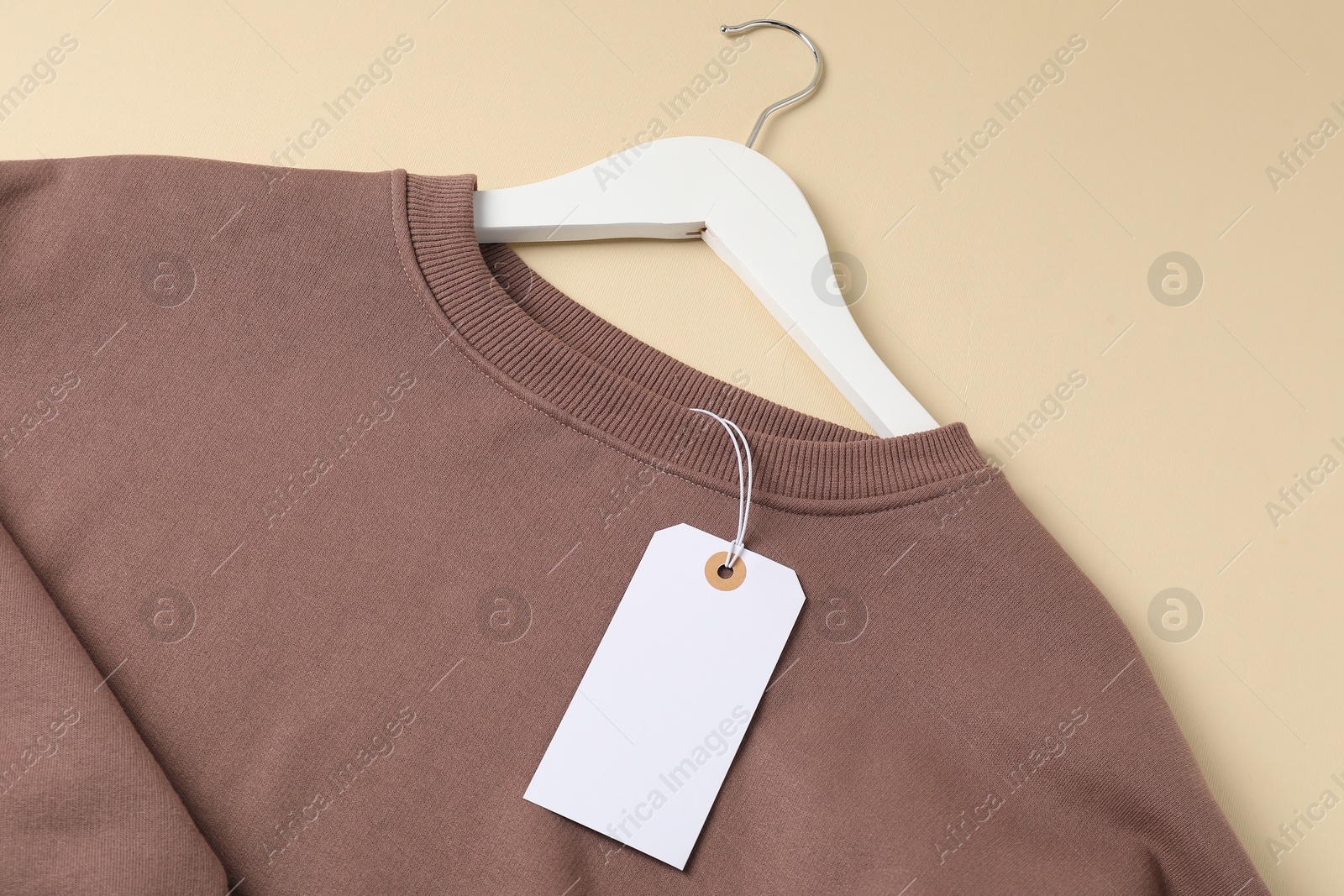 Brown garment with tag on beige background, top view Photo of Brown garment with tag on beige background, top view
