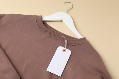 Photo of Brown garment with tag on beige background, top view
