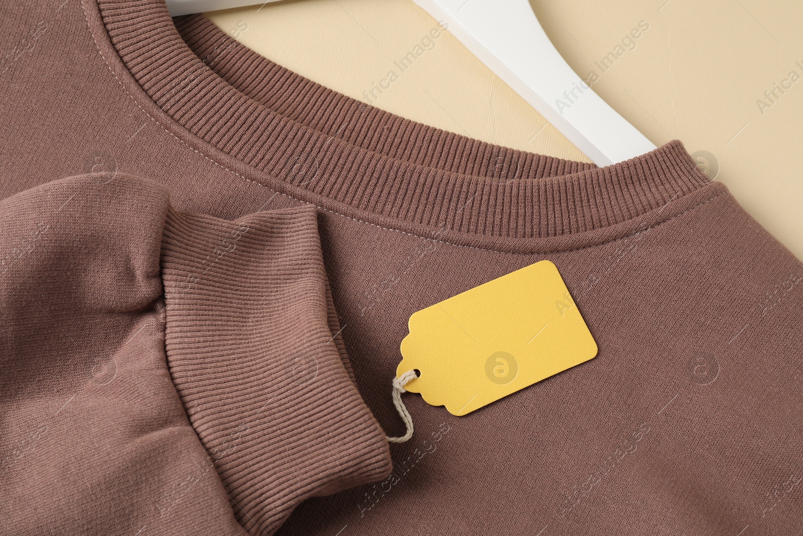 Brown garment with tag on beige background, above view Photo of Brown garment with tag on beige background, above view
