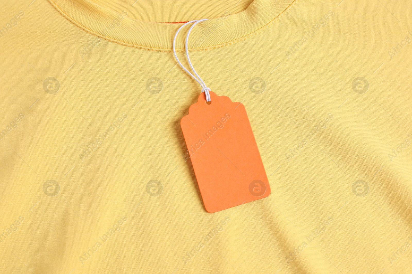Cardboard tag on yellow garment, top view Photo of Cardboard tag on yellow garment, top view