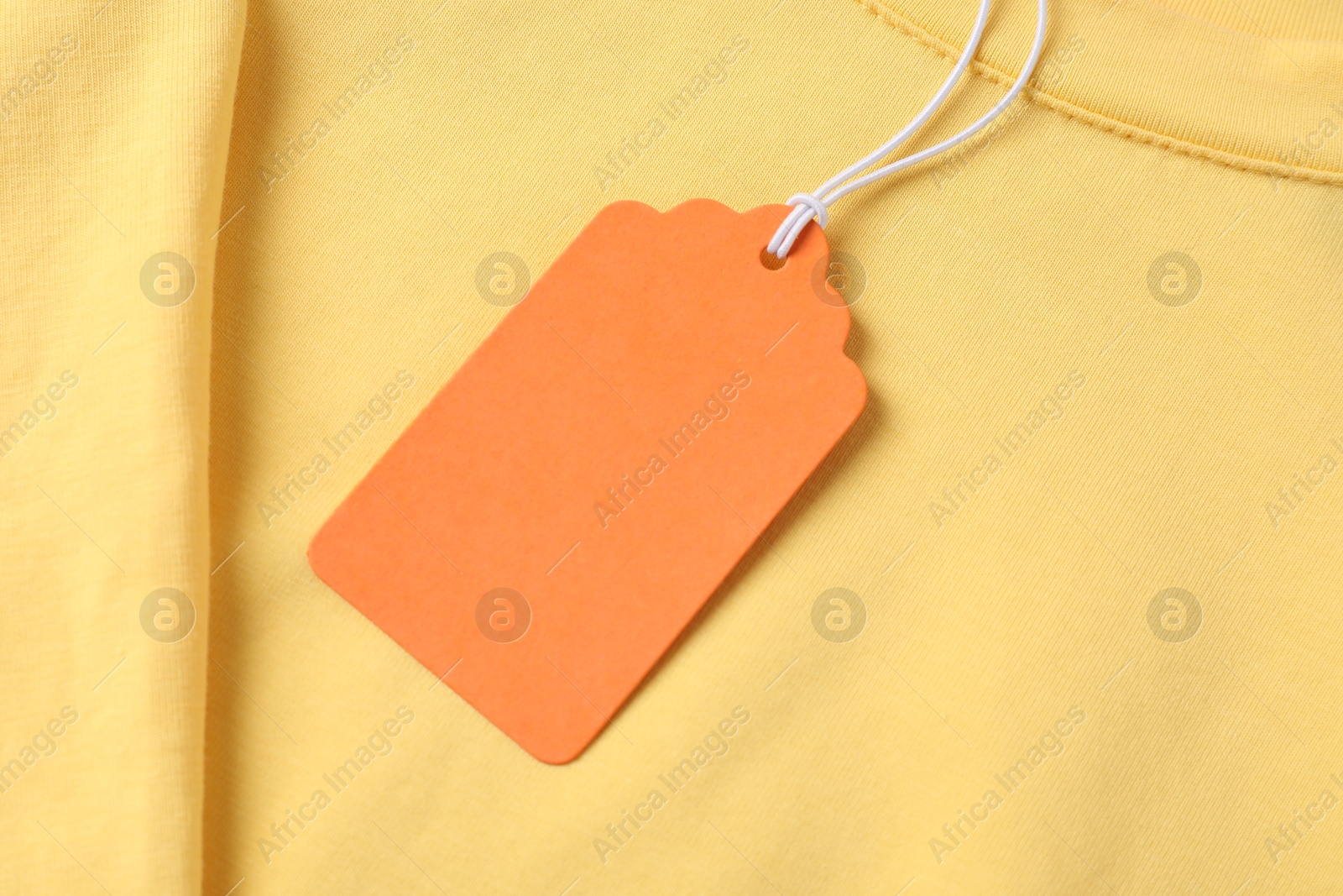 Cardboard tag on yellow garment, top view Photo of Cardboard tag on yellow garment, top view