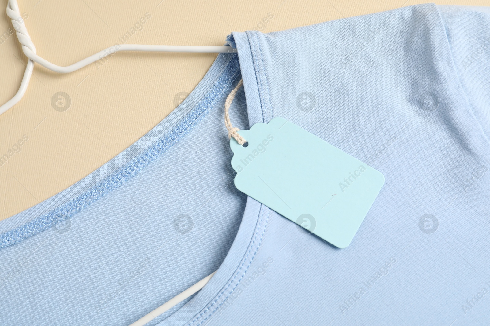 Light blue t-shirt with tag on beige background, top view Photo of Light blue t-shirt with tag on beige background, top view