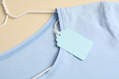 Photo of Light blue t-shirt with tag on beige background, top view