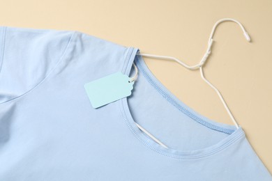 Photo of Light blue t-shirt with tag on beige background, top view
