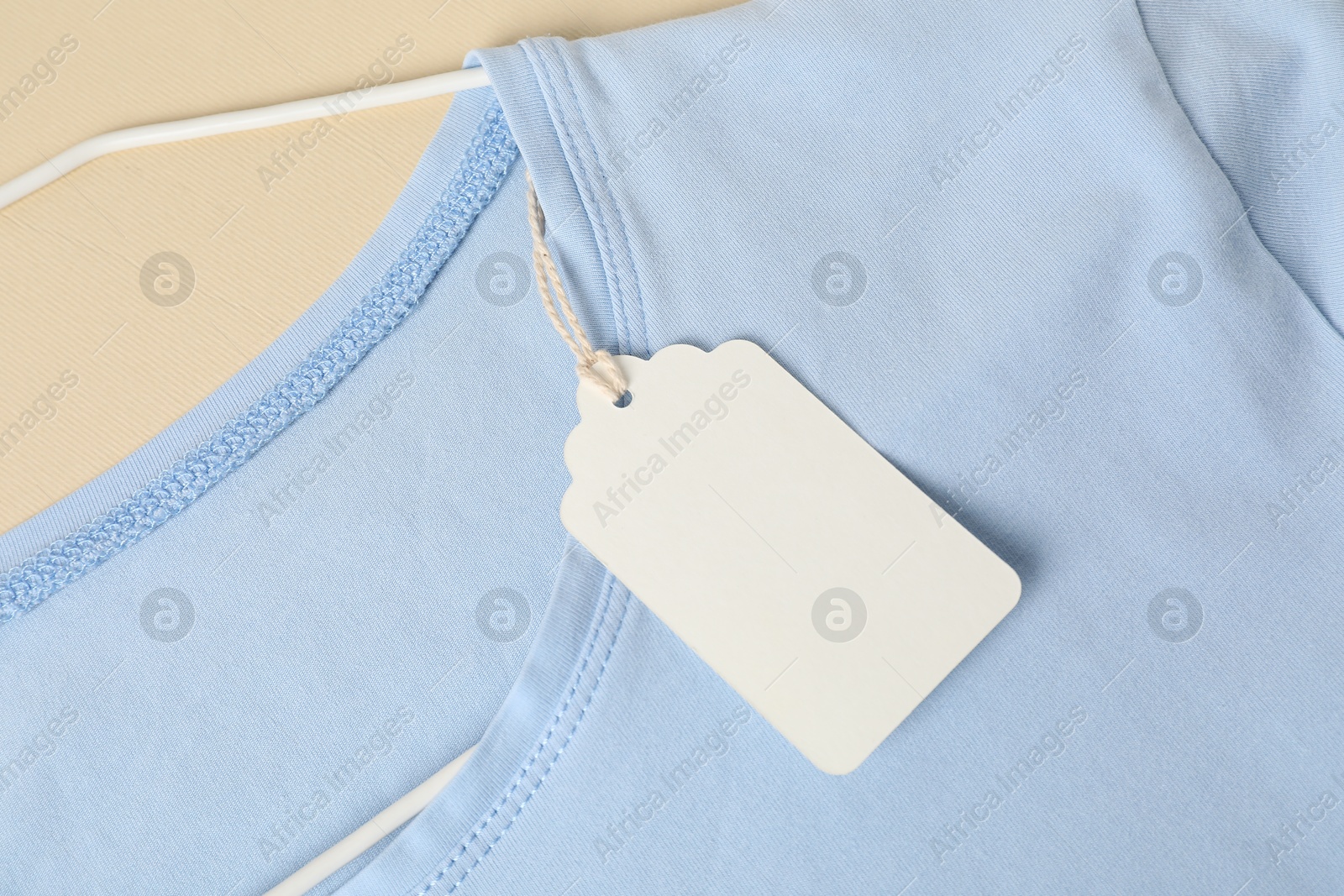 Light blue t-shirt with tag on beige background, top view Photo of Light blue t-shirt with tag on beige background, top view