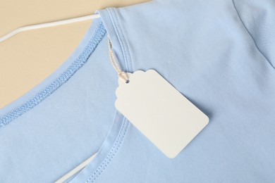 Photo of Light blue t-shirt with tag on beige background, top view