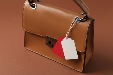 Photo of Leather bag with tags on brown background, closeup
