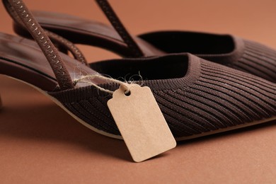 Photo of Elegant shoes with tag on brown, closeup
