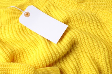 Photo of Cardboard tag on yellow knitted sweater, above view