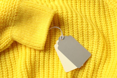 Photo of Cardboard tags on yellow knitted sweater, top view