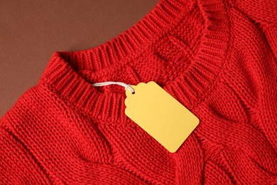 Photo of Red knitted sweater with tag on brown background, top view