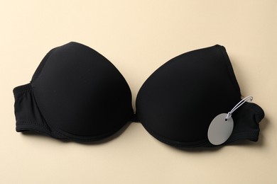 Photo of Black bra with tag on beige background, top view